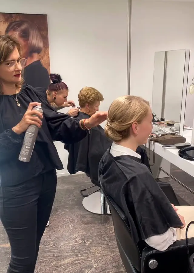Im Salon: Eine Stylistin fixiert eine Hochsteckfrisur mit Haarspray