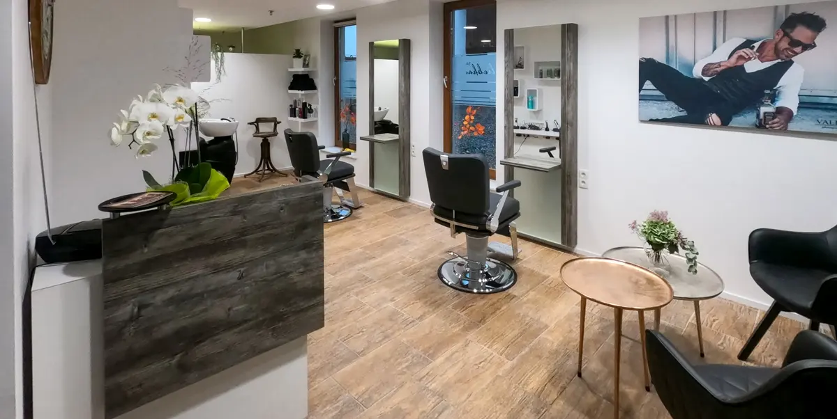 Der Salon: Empfang mit Orchideen, zwei Barber-Stühle vor hohen Spiegeln, Sessel im Wartebereich